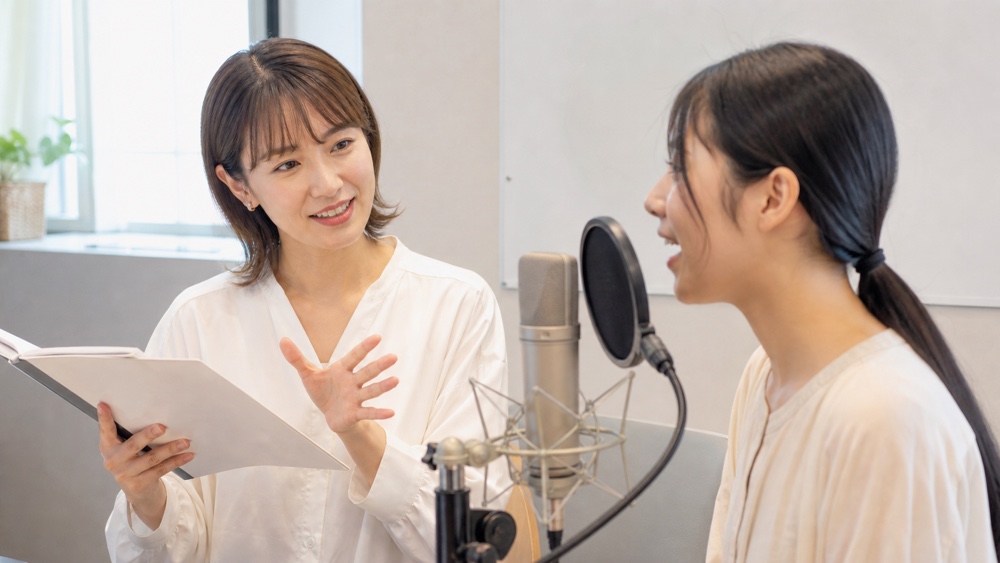 マイクの前で講師のレッスンを受ける声優志望の女性