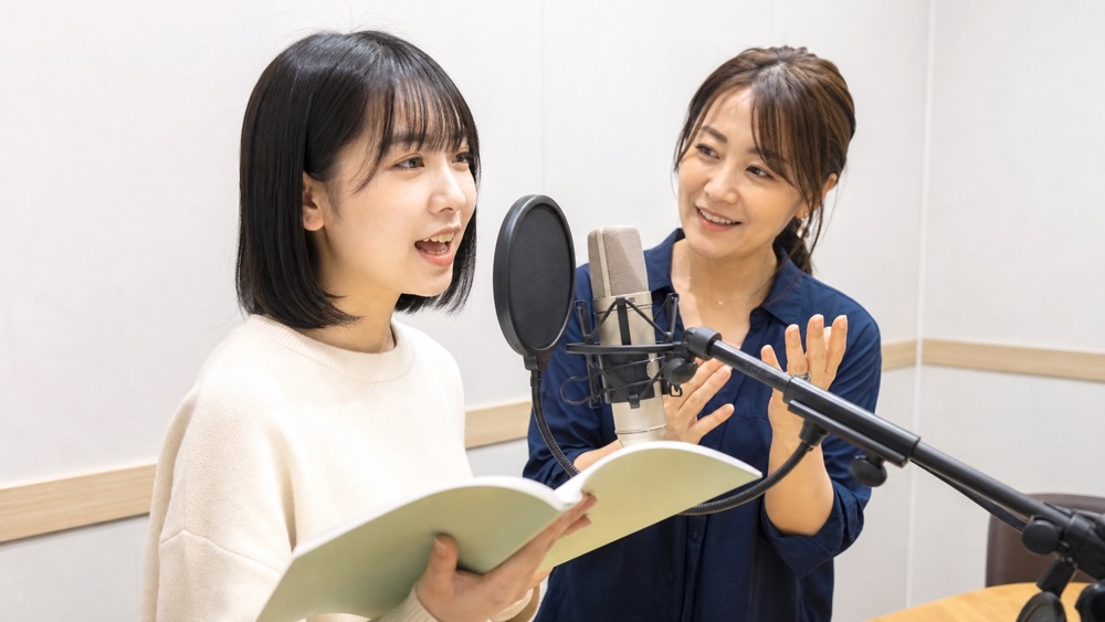 マイクの前で講師のレッスンを受ける声優志望の女性