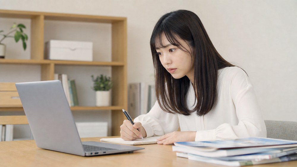 神戸の声優専門学校の情報をノートパソコンと資料で確認する女性