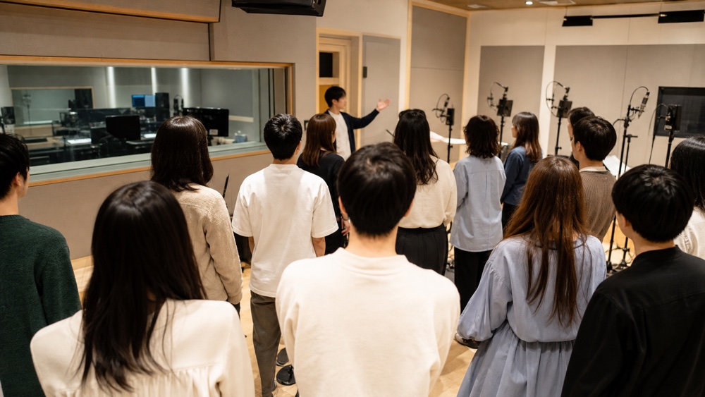 多数の所属声優が録音スタジオで説明を受けるイメージ