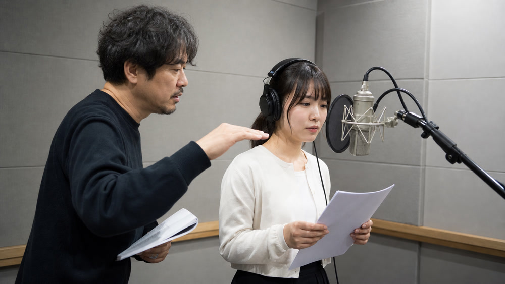 録音ブースで講師からマイク練習の指導を受ける生徒