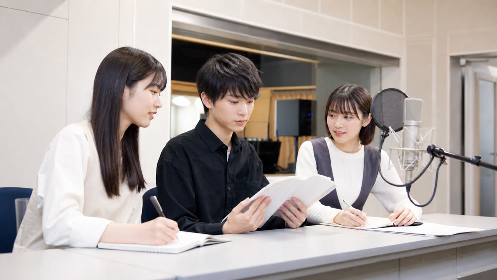 収録ブースで台本を確認しながら声優レッスンを受ける学生