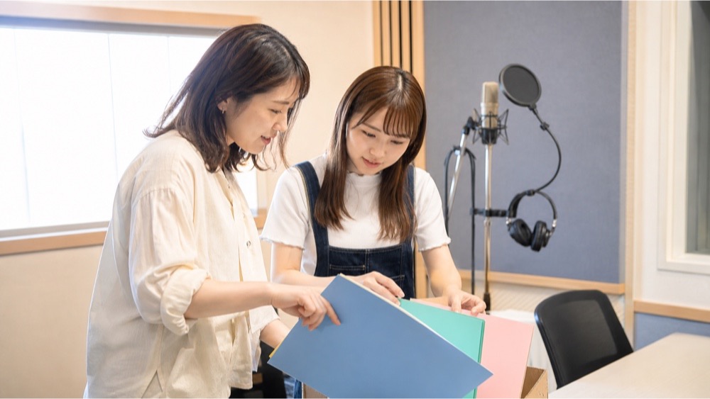 声優レッスン室で進路別の資料を整理する講師と学生