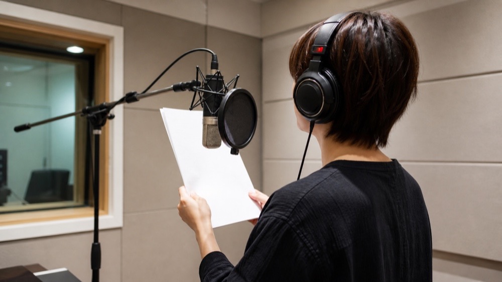 レコーディングブースで台本を読みながら収録する声優のイメージ