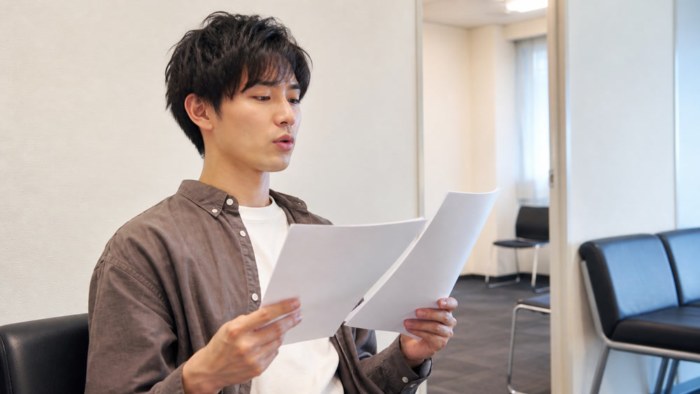 声優事務所のオーディション待機室で応募書類を確認する志望者