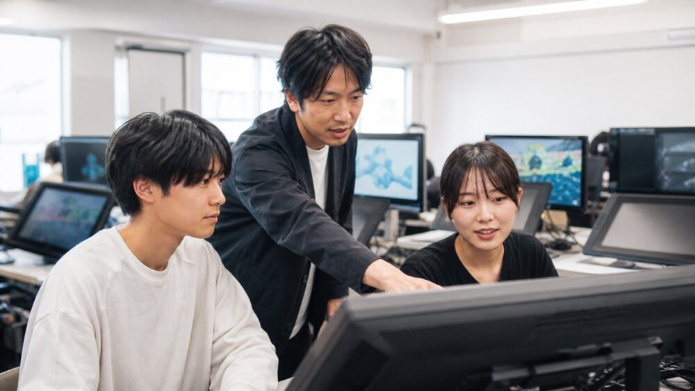 ゲーム制作画面を見ながら講師の実務指導を受ける学生