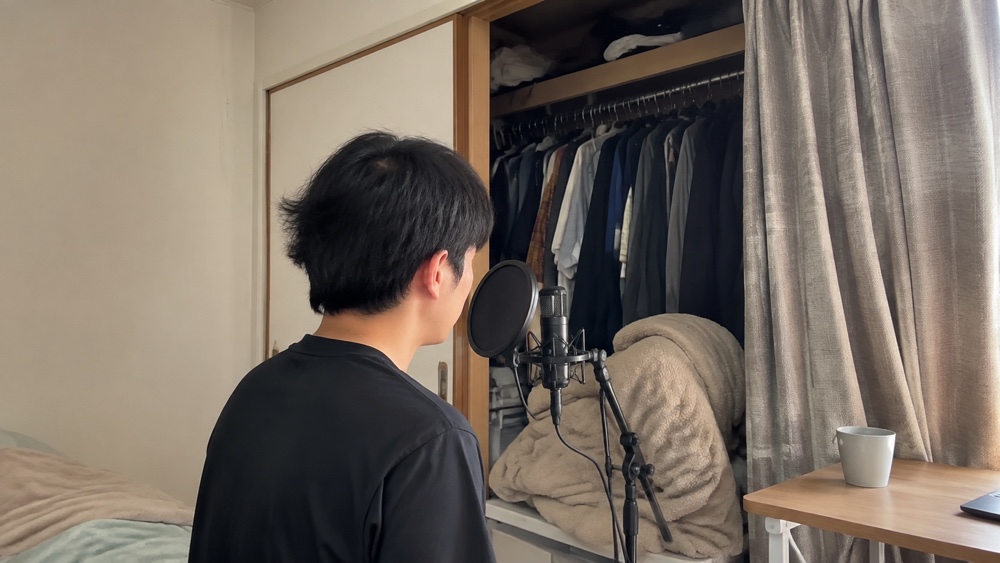 衣類の入ったクローゼットと厚手のカーテンを使って自宅録音する様子