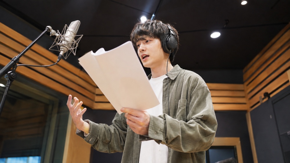 録音ブースで話す速さと語尾を意識して台本を読む男性