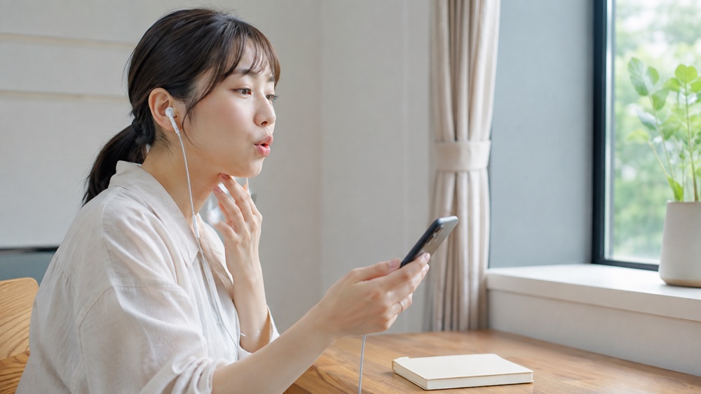 イヤホンでお手本音声を聞きながら発声練習する女性