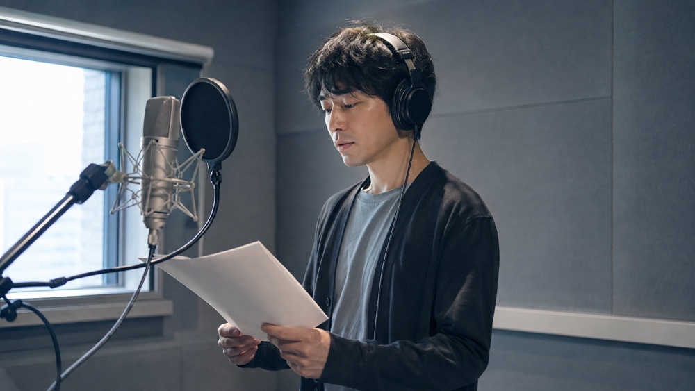 静かな収録ブースで落ち着いたナレーションを読む男性