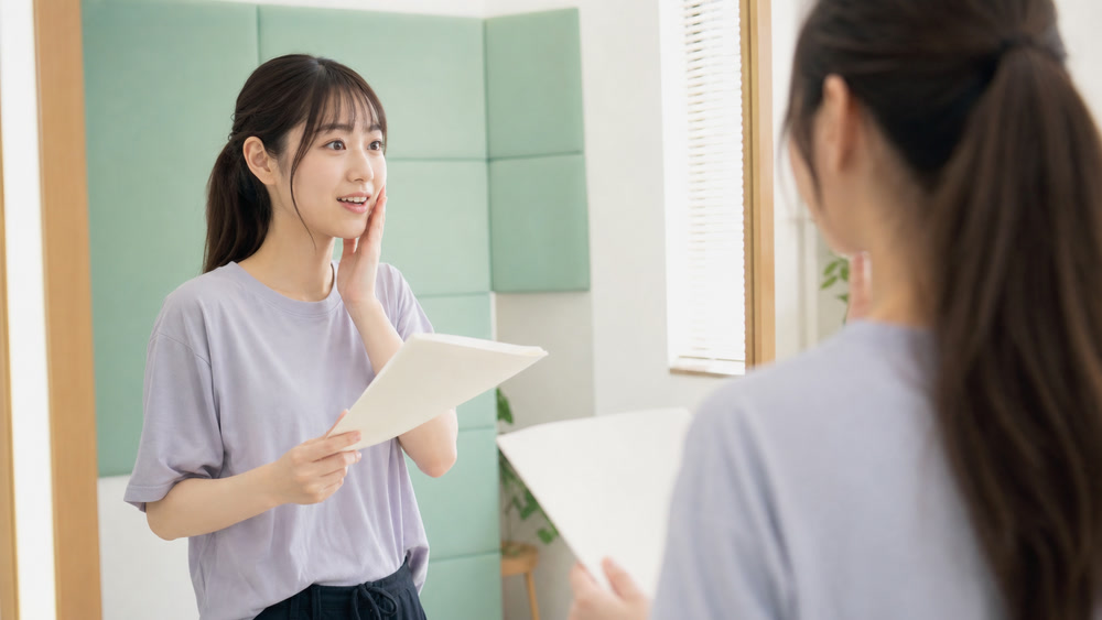 鏡の前で喜びと戸惑いと照れの表情を練習する女性