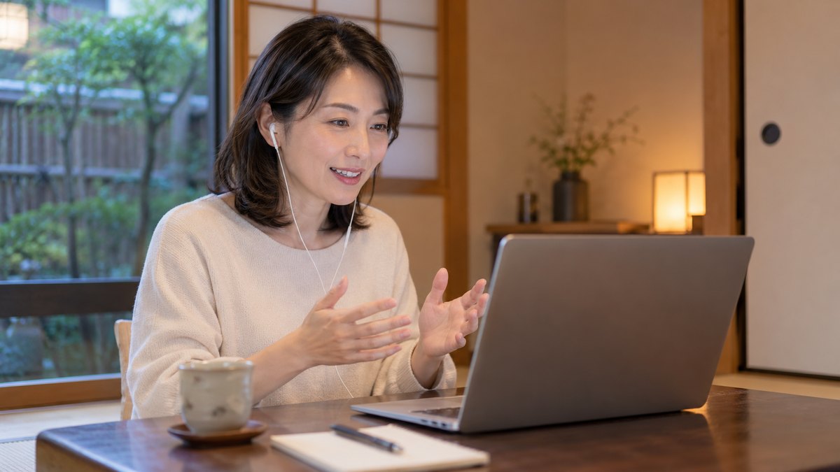 平日の夜、自宅の和室の座卓で、40代の女性がノートパソコンに向かってイヤホンをつけ、背筋を伸ばして画面の向こうの講師と話している近景。パソコンの画面は見えない角度