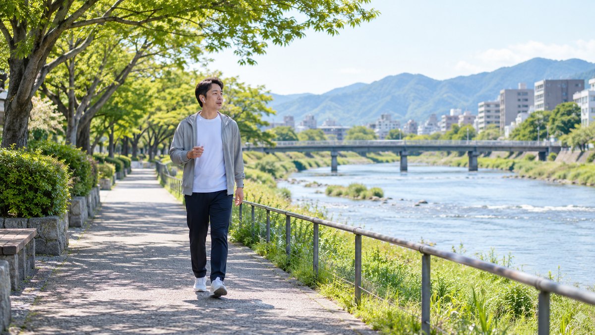 休日の朝、川沿いの遊歩道で、40代の男性がイヤホンをつけてゆっくり歩きながら、小さく口を動かして声を出す練習をしている遠景。文字は無い