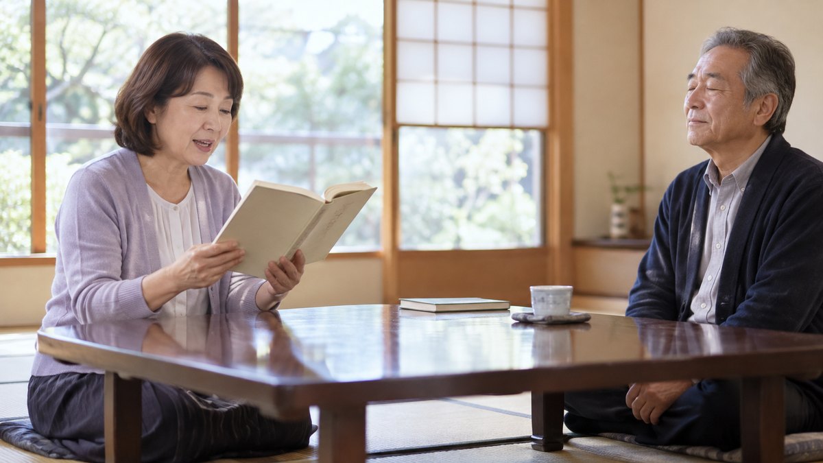 週末の午後、地域の公民館の明るい和室で、50代の女性が座卓の前に正座して本を両手で持ち、朗読の練習会で声に出して読んでいて、向かいに座る60代の男性の講師が目を閉じて聞いている近景。本や壁に文字は見えない