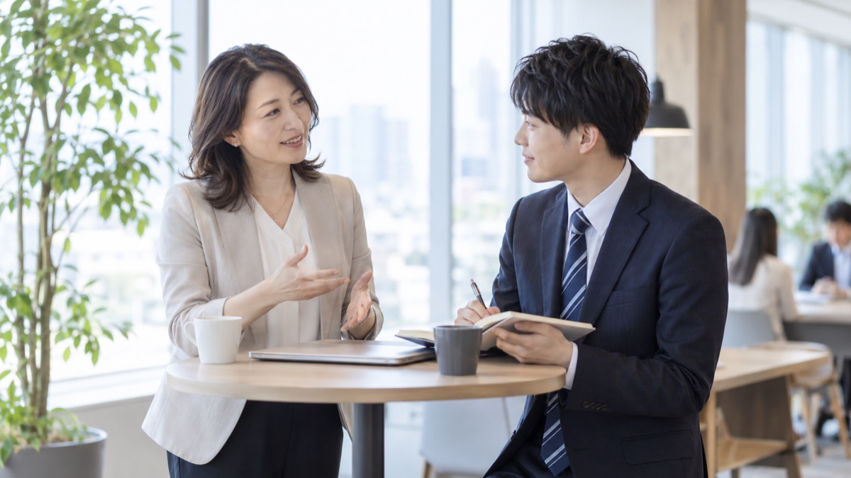 立ち話用のテーブルで後輩に話し方を助言する先輩社員