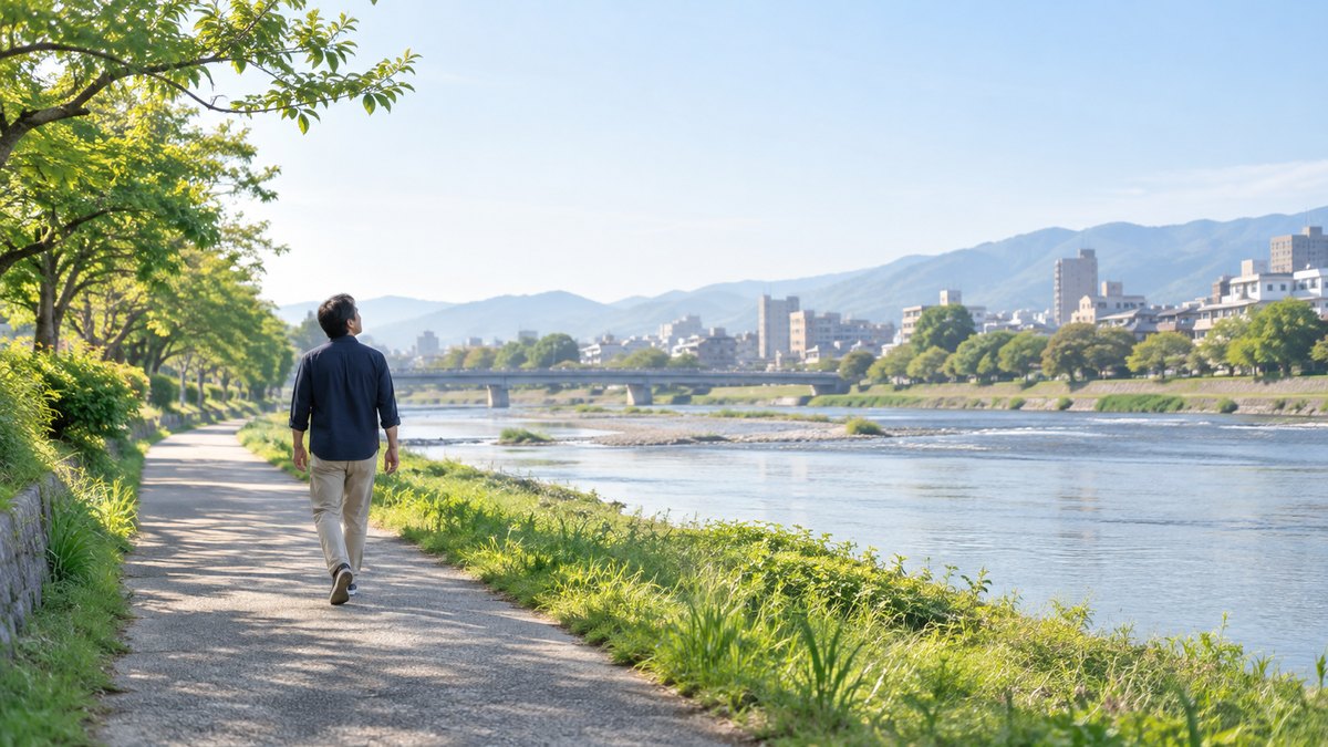 休日の朝、川沿いの遊歩道で、40代の男性がゆっくり歩きながら深く息を吸っている遠景。顔ははっきり写らない。文字は無い