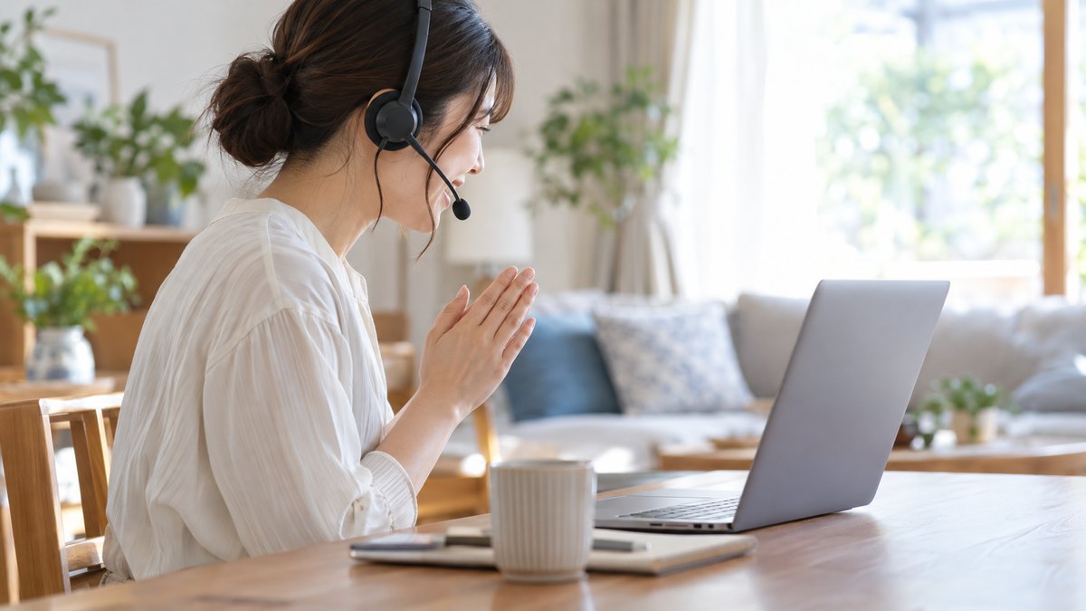 朝、在宅勤務の自宅のリビングの机で、30代の女性がヘッドセットをつけてノートパソコンに向かい、会議の始まりに笑顔で軽く会釈している横からの近景。画面は見えない角度。顔ははっきり写らない。文字は無い