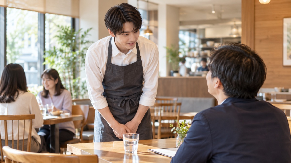 レストランのテーブル席で男性客に頭を下げて話を聞く店員