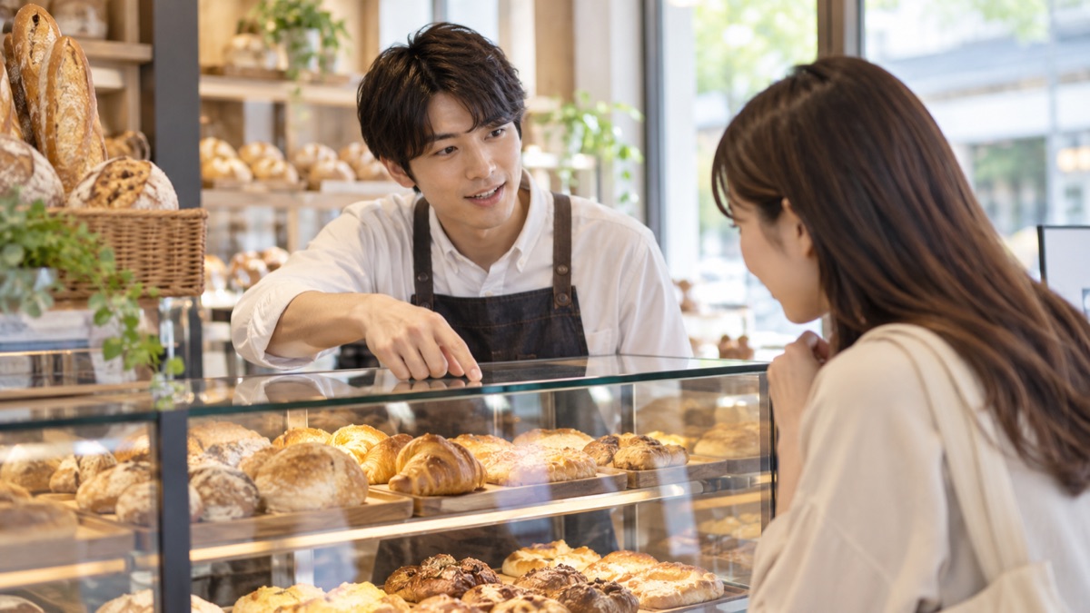 ベーカリーのショーケース越しに女性客へ説明する店員