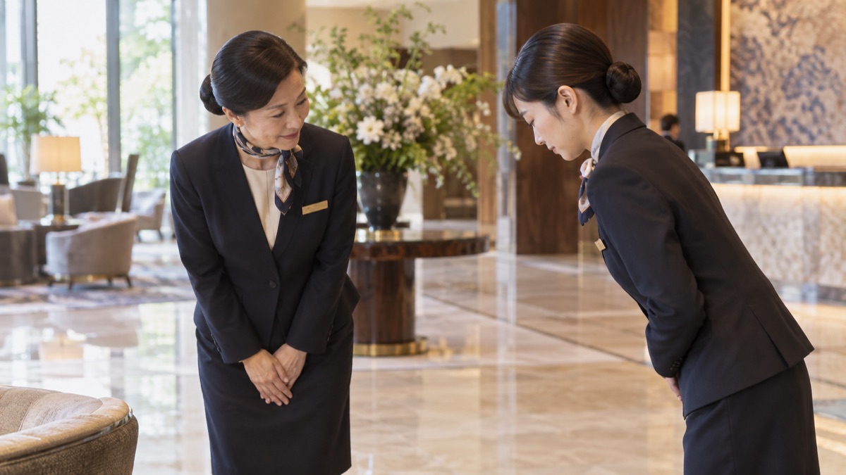 ホテルのロビーでベテランスタッフが新人に接客の手本を見せる様子