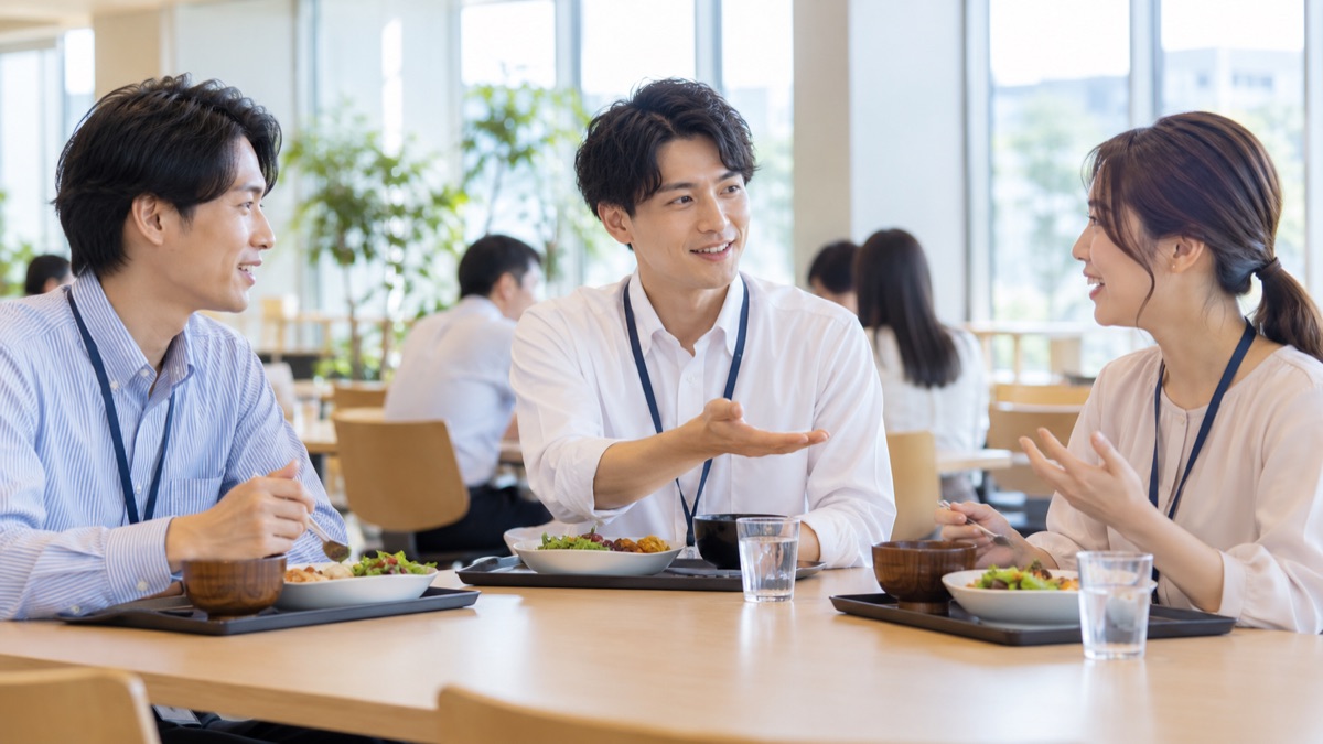 社員食堂のテーブルで、若手の男性社員が同僚2人の意見を順番に聞いている