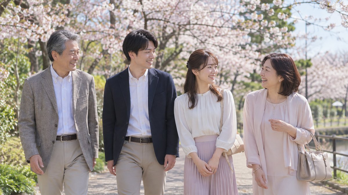春の昼、桜の咲く公園の遊歩道を、婚約した20代後半の男女と男性の両親が並んでゆっくり歩き、母親が笑いながら婚約者の女性に話しかけている