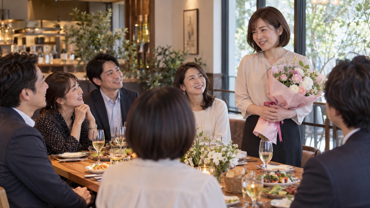 送別会の主役が花束を胸に抱えて立ち、同僚たちに向かってお礼の挨拶をしている