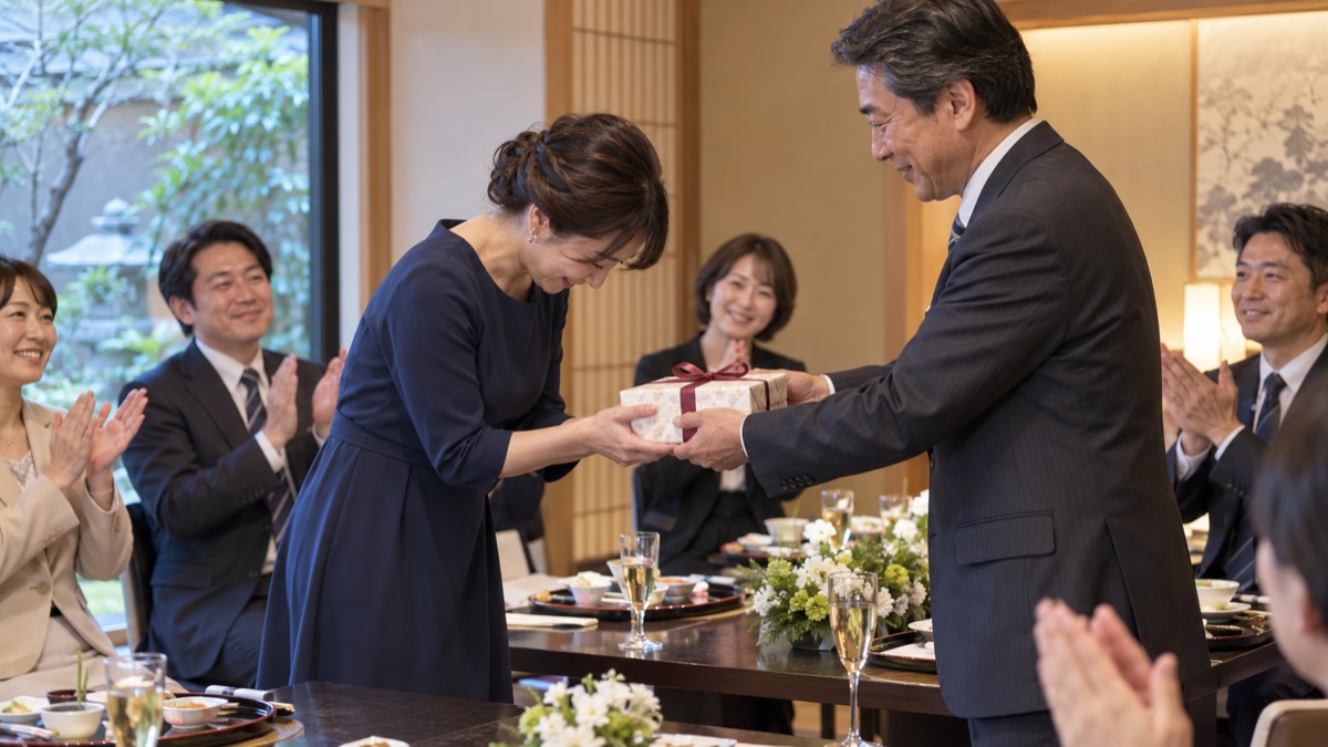 送別会の主役が記念品の包みを受け取り、深くお辞儀をしている