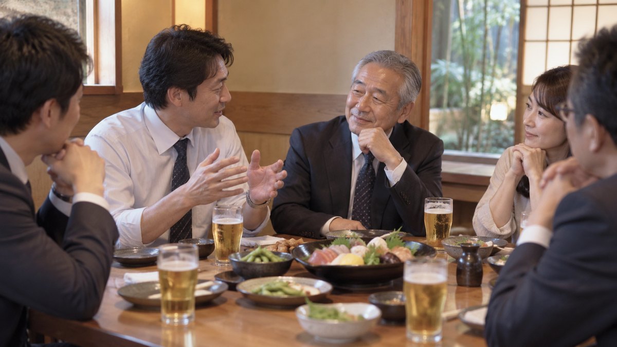 居酒屋の掘りごたつの座敷で、40代の男性社員が座ったまま体を横に向け、隣に座る60代の主役の男性に思い出を語りかけている。主役は目を細めて聞き、向かいの同僚たちも静かに聞いている