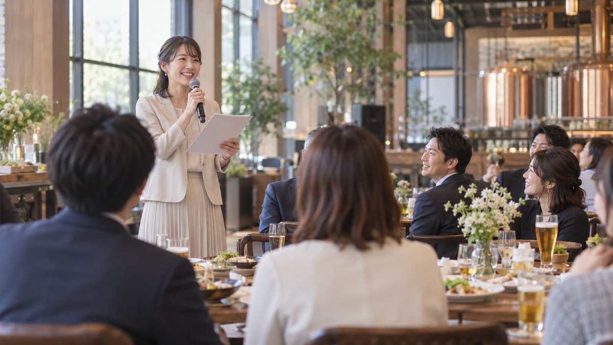 天井の高いビアレストランの貸切スペースで、30代の女性司会者がマイクを持ち、紙の台本を胸の高さに持って、テーブルに着いた社員たちに笑顔で話し始めている