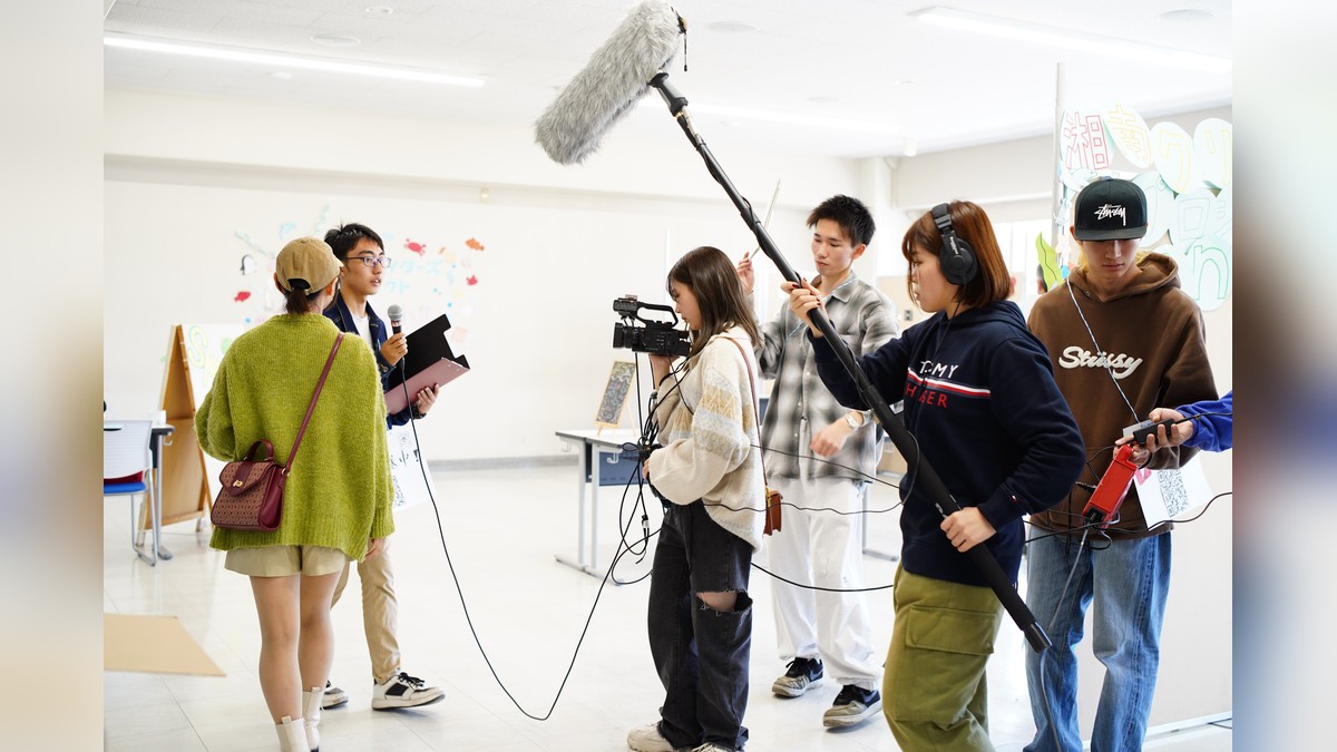 テレビ班の学生が学内イベントでマイクを使って出演者にインタビューしている様子