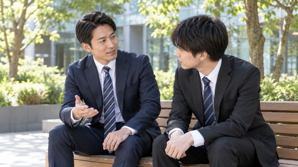 会社の中庭のベンチで先輩社員が落ち込んだ新入社員にやさしく話しかける