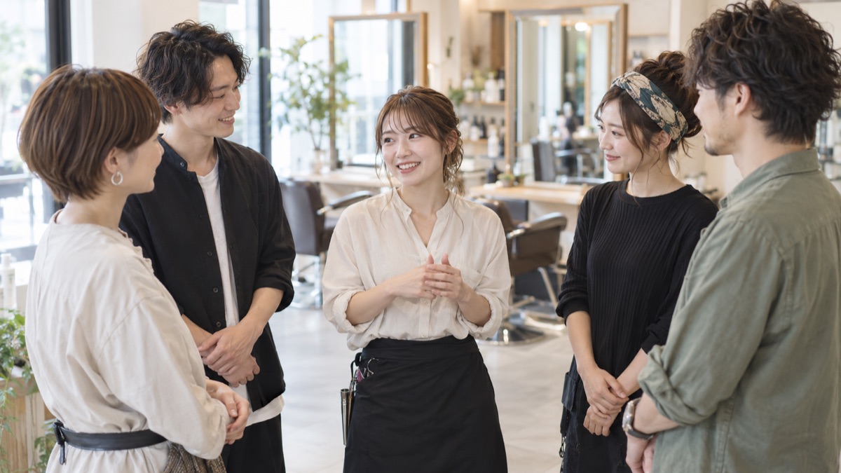 開店前の美容室の朝礼で笑顔で話すスタッフとうなずく仲間