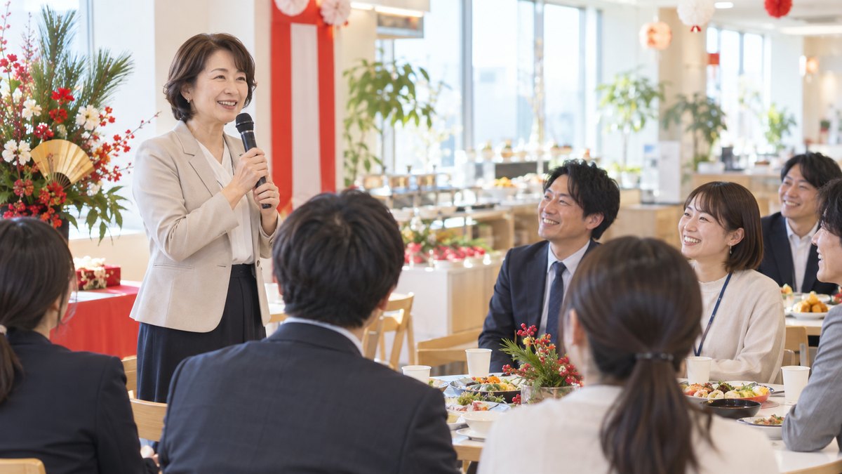昼の明るい社員食堂を飾りつけた新年会で、50代の女性部長がマイクを持って穏やかに話し、テーブルの社員たちが笑顔で聞いている