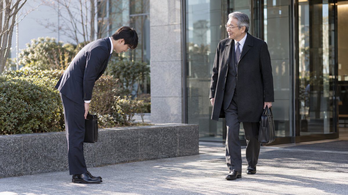 1月の朝、本社の玄関前の植え込みのそばで、20代の男性社員が立ち止まり、出社してきた60代の男性社長に頭を下げて挨拶している