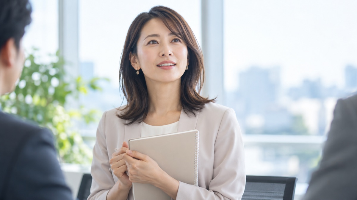 会議室の窓際でノートを持ち、意見を話そうと前を向く女性社員