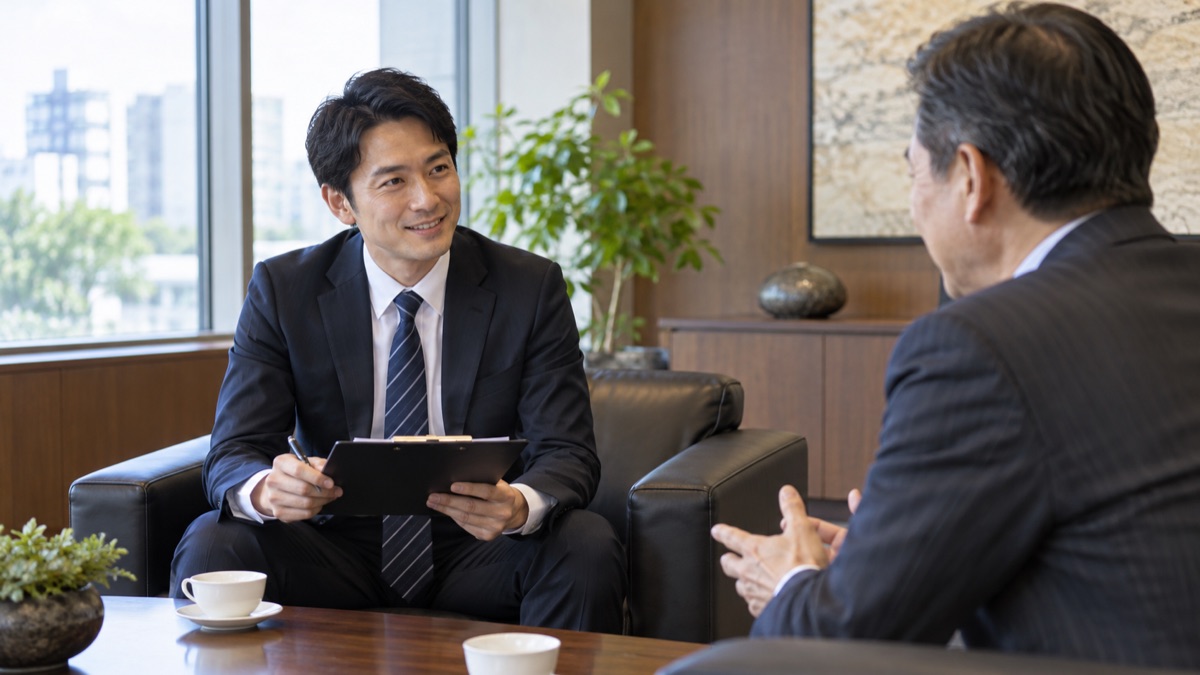 取引先の応接室で、お客様の話を笑顔で聞く営業担当の男性