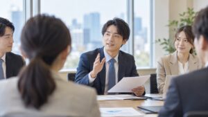 定例会議で資料を手に、穏やかな表情で手を挙げて質問しようとする男性社員