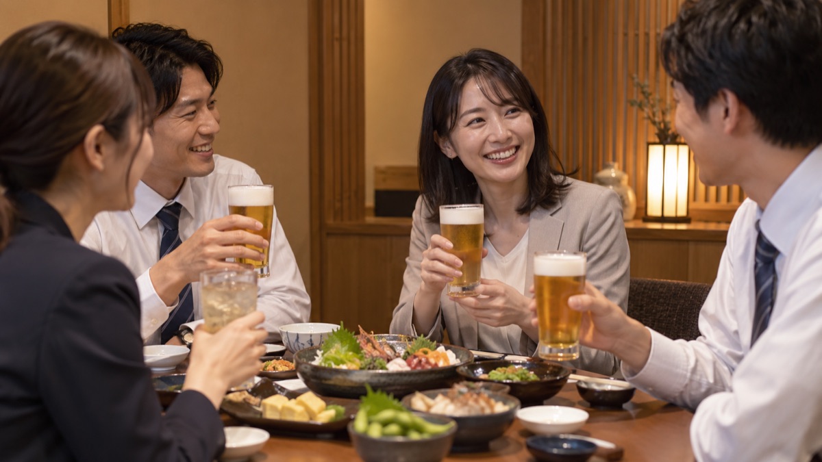 仕事帰りの居酒屋で、同僚と乾杯のあとに笑顔で話す女性会社員