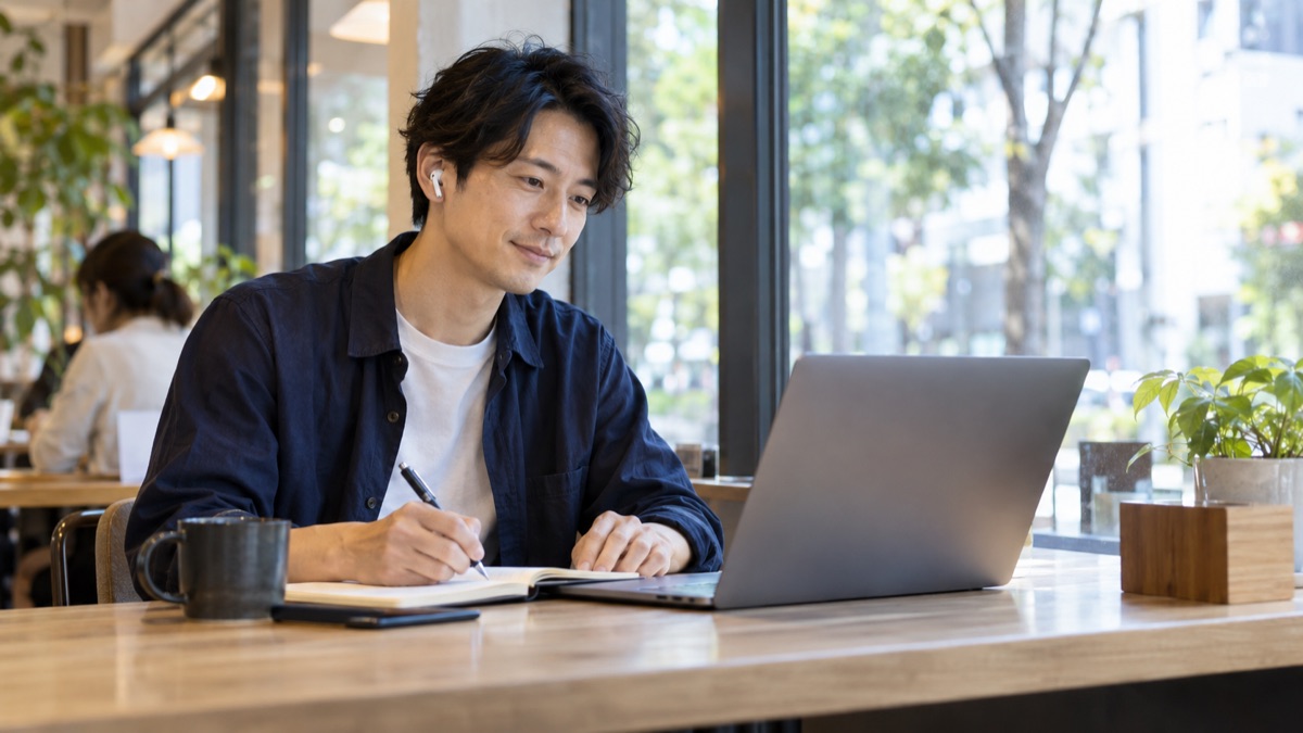 カフェでオンラインの講義を見ながらメモを取る男性