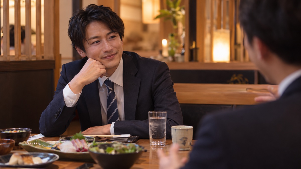 仕事帰りの食事の席で同僚の話を聞く男性
