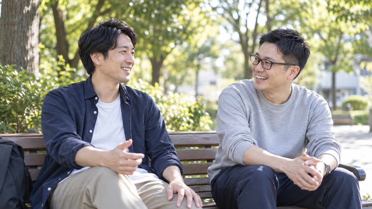 休日の公園のベンチで友人と話す男性