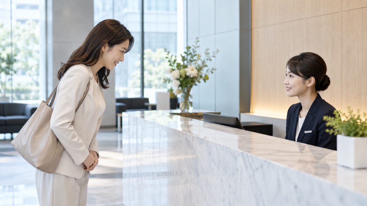 オフィスビルの受付カウンターで、受付の担当者に会釈して名乗る30代の女性