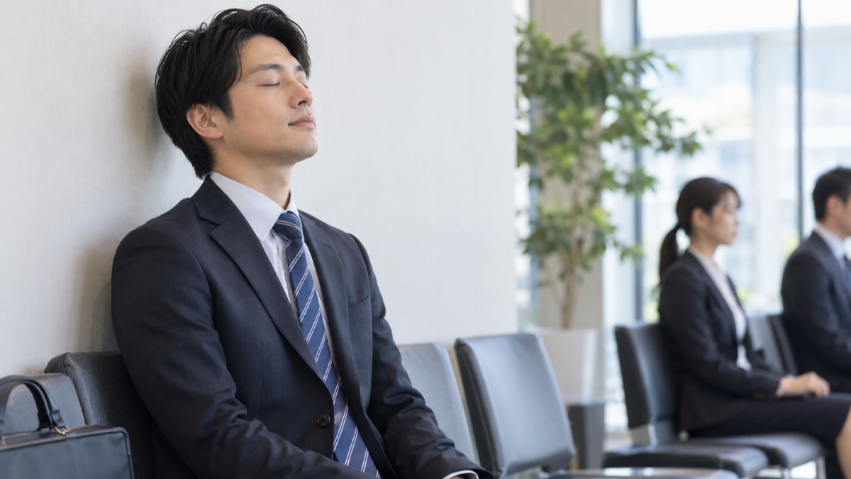 面接会場の待合スペースの椅子で、目を閉じてゆっくり息を吐き気持ちを整える30代の男性
