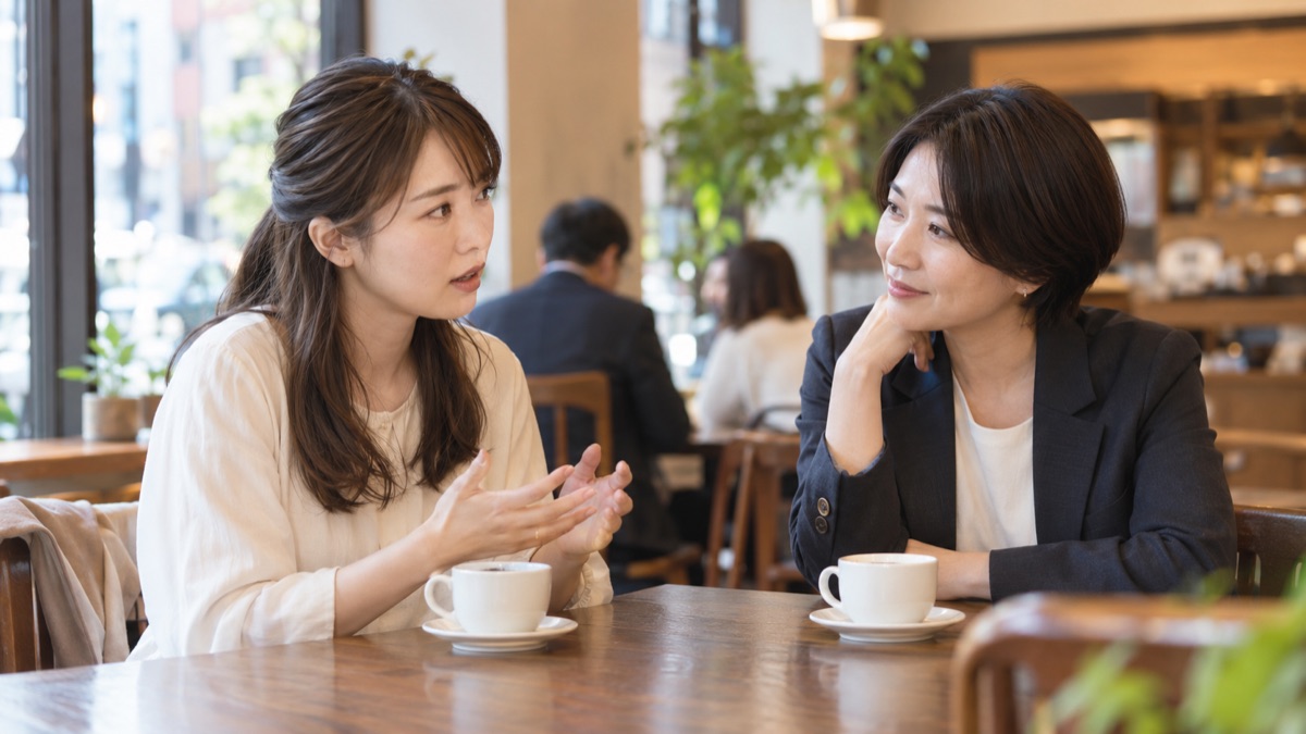 駅前の喫茶店で、先輩に面接の不安を打ち明け、うなずきながら話を聞いてもらう20代後半の女性