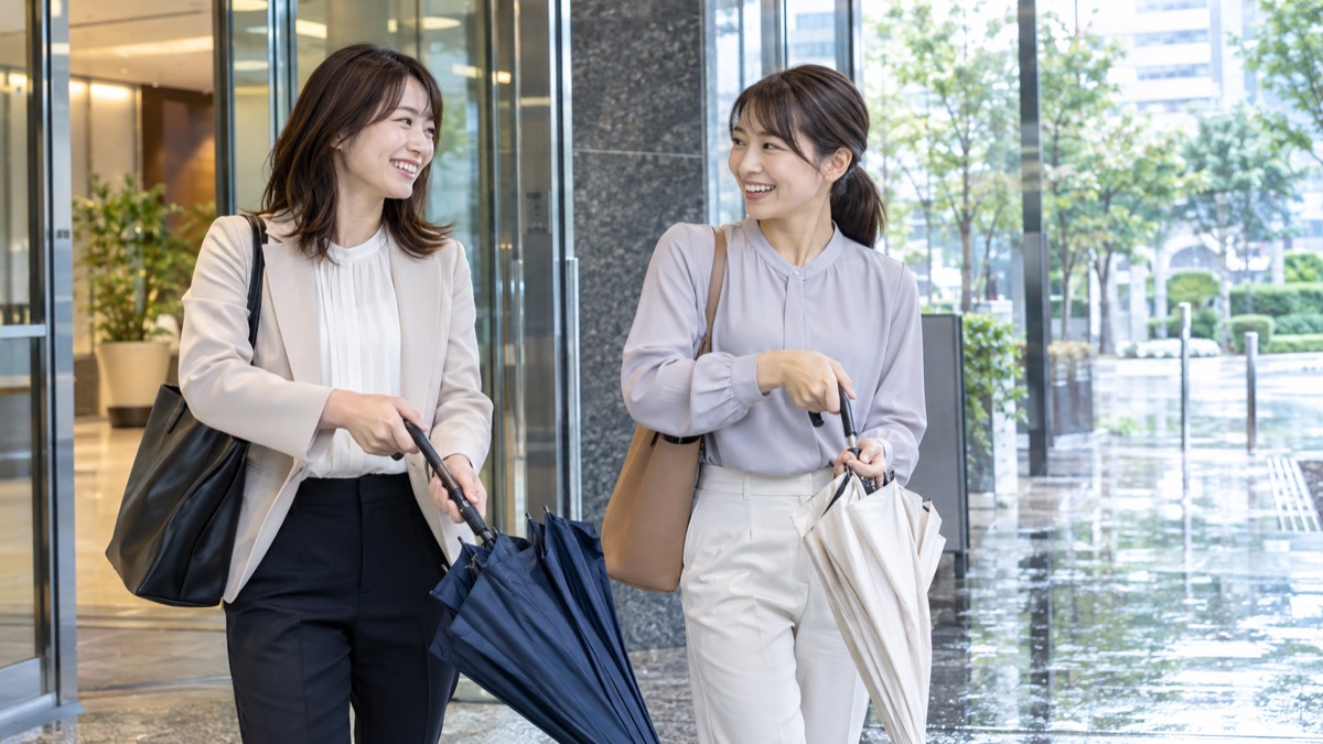 雨上がりのビルの入口で傘をたたみながら話す女性社員2人