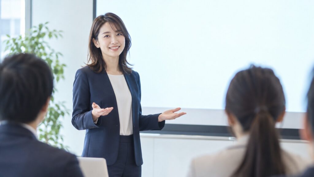 会議室で聞き手の方へ体を向け、手のひらを上に向けてプレゼンをする女性