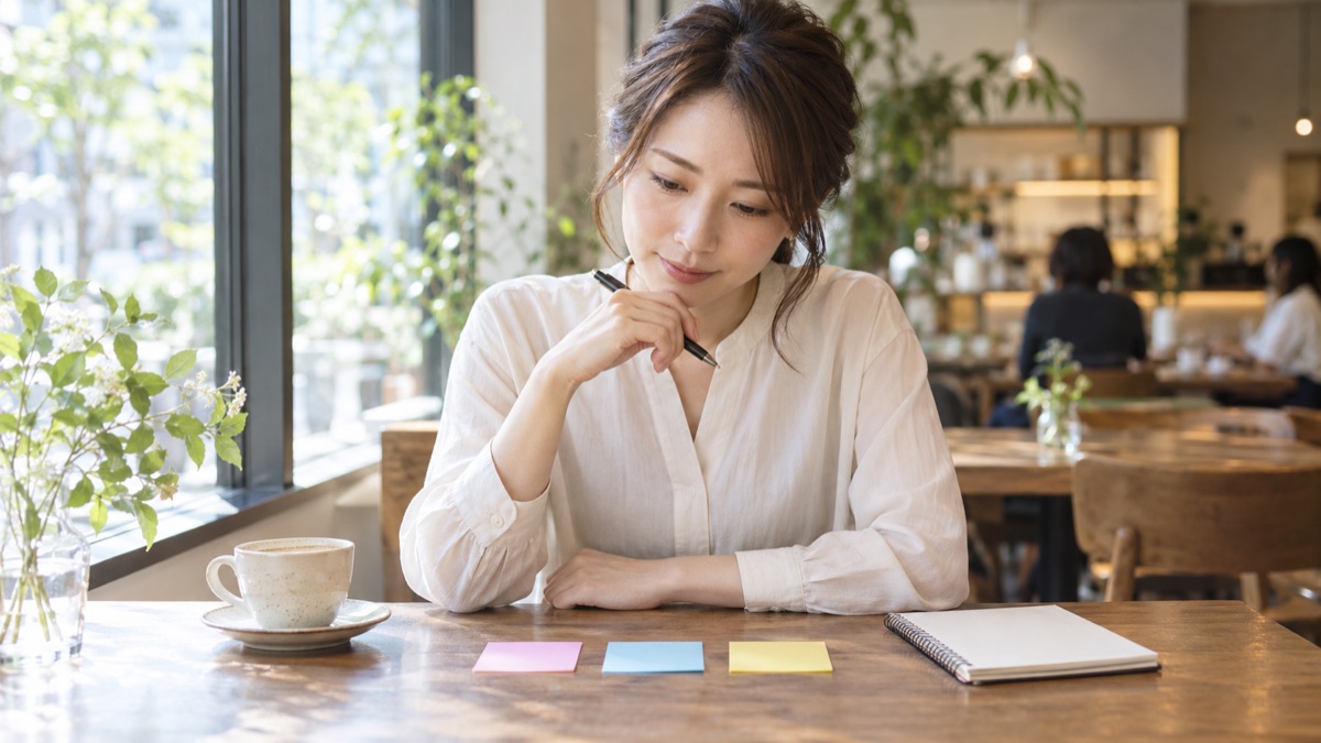 カフェで付箋を3枚並べて話す順番を考える女性