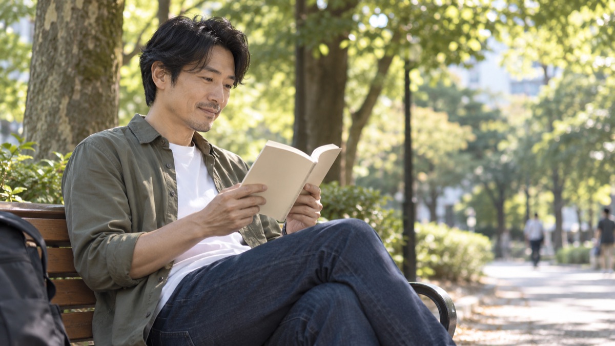 休日の公園のベンチで、文庫本の小説を読む男性