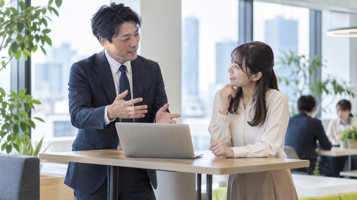 オフィスの打ち合わせスペースで、後輩にやさしく説明する男性会社員